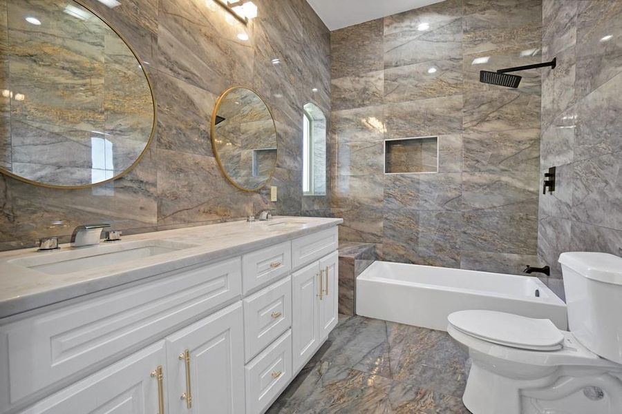 Full bathroom featuring tiled shower / bath, vanity, toilet, and tile walls