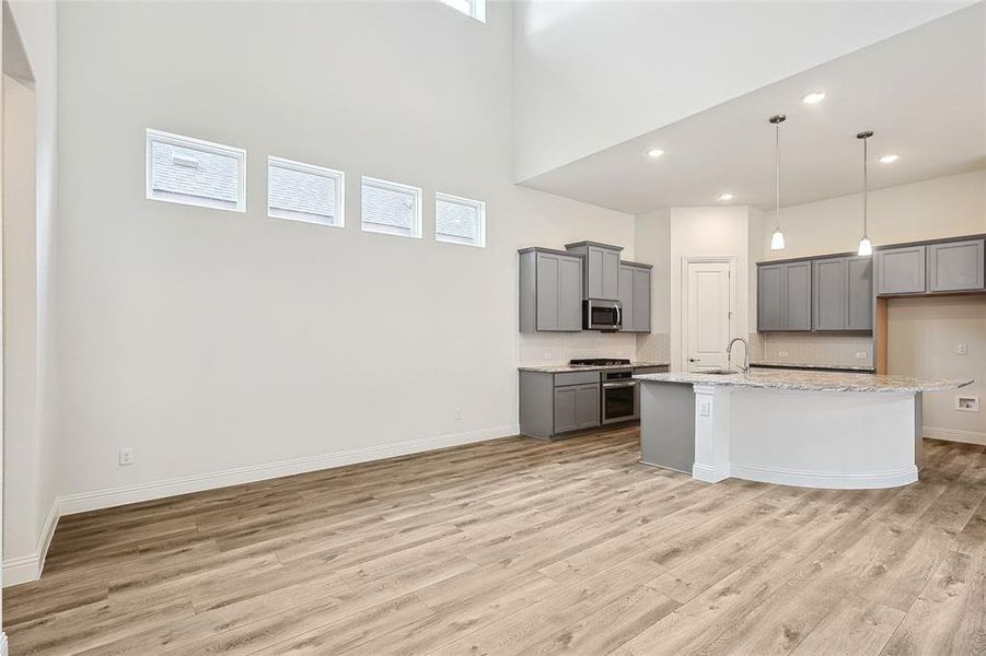 Kitchen with an island with sink, gray cabinetry, a healthy amount of sunlight, light stone counters, and light hardwood / wood-style floors