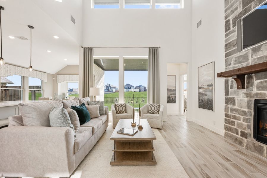 Living room with two-story ceiling, stone fireplace, and large windows overlooking backyard