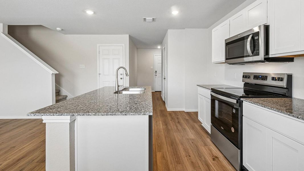 A contemporary kitchen boasts granite countertops, stainless steel appliances, and sleek wood flooring, ready for culinary endeavors.