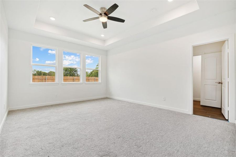 Empty room with a tray ceiling, ceiling fan, and carpet floors