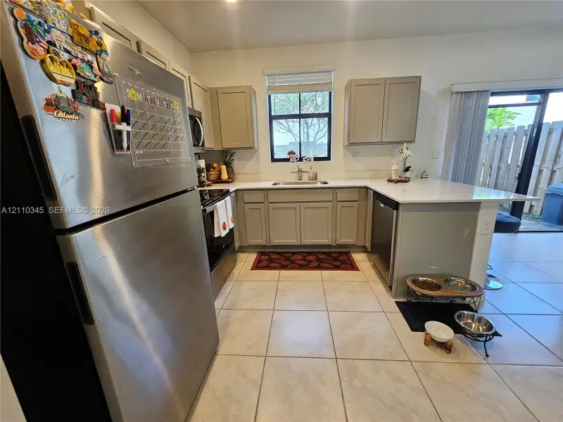 Kitchen featuring light gray shaker-style cabinetry, white quartz countertops, stainless steel appliances, ceramic tile flooring, and a window above the undermount sink