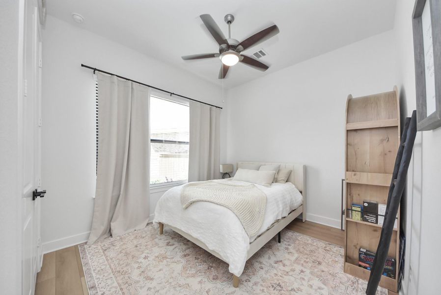 Cozy bedroom featuring a large window for natural light, elegant ceiling fan, and a stylish wooden bookshelf, all complemented by a soft area rug.