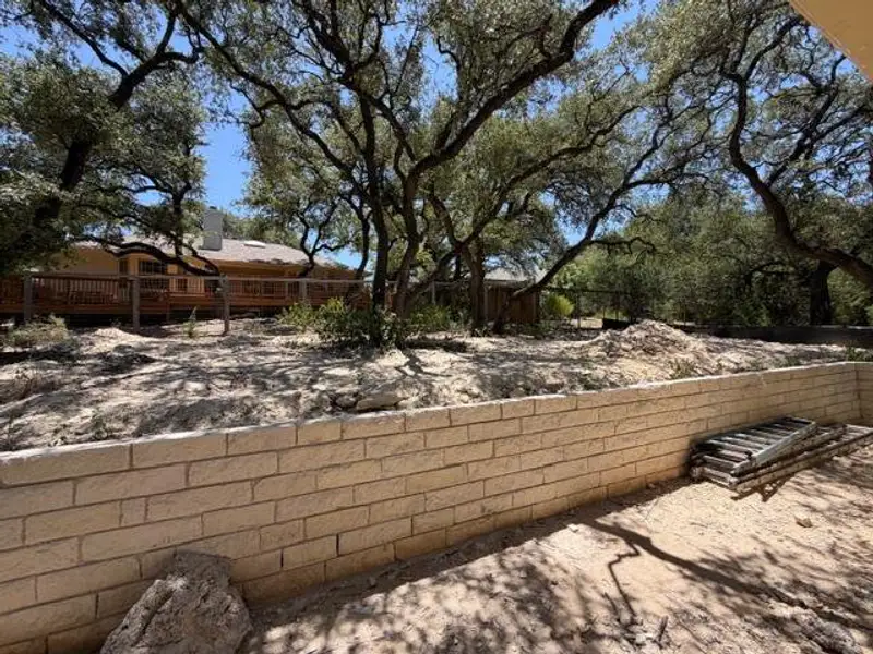 Mature trees canopy the yard, leading to a home with a covered patio and a stone retaining wall. Mature trees canopy the yard, leading to a home with a covered patio and a stone retaining wall.