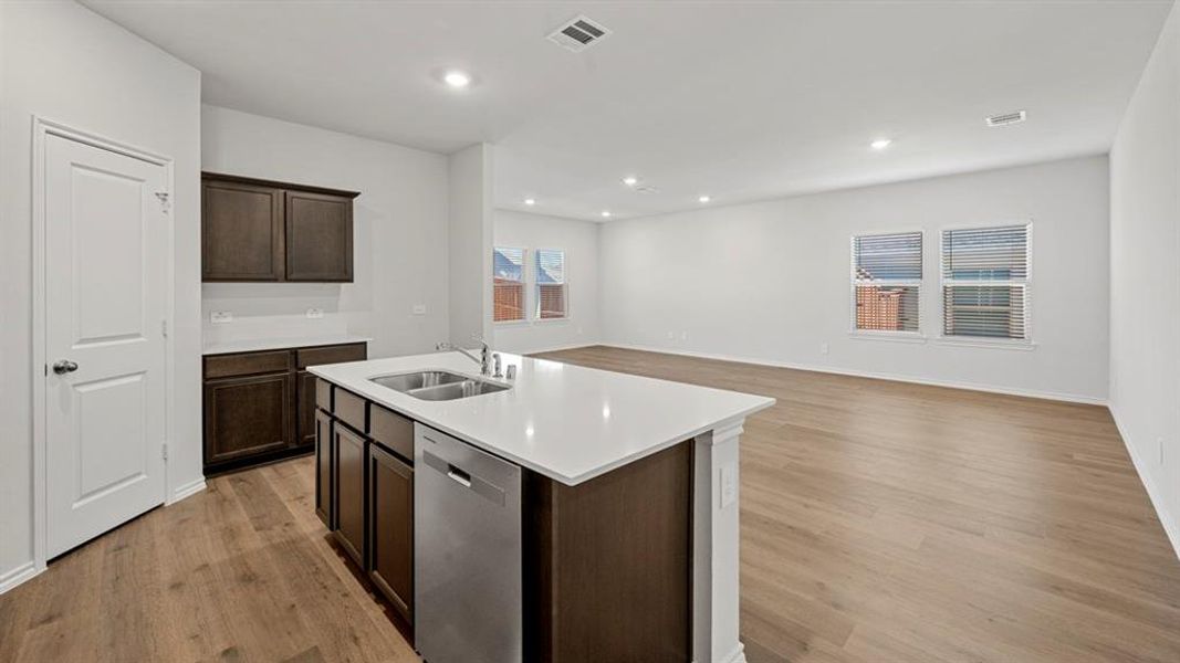 Kitchen with dark brown cabinetry, a center island with sink, open floor plan, stainless steel dishwasher, and light wood finished floors
