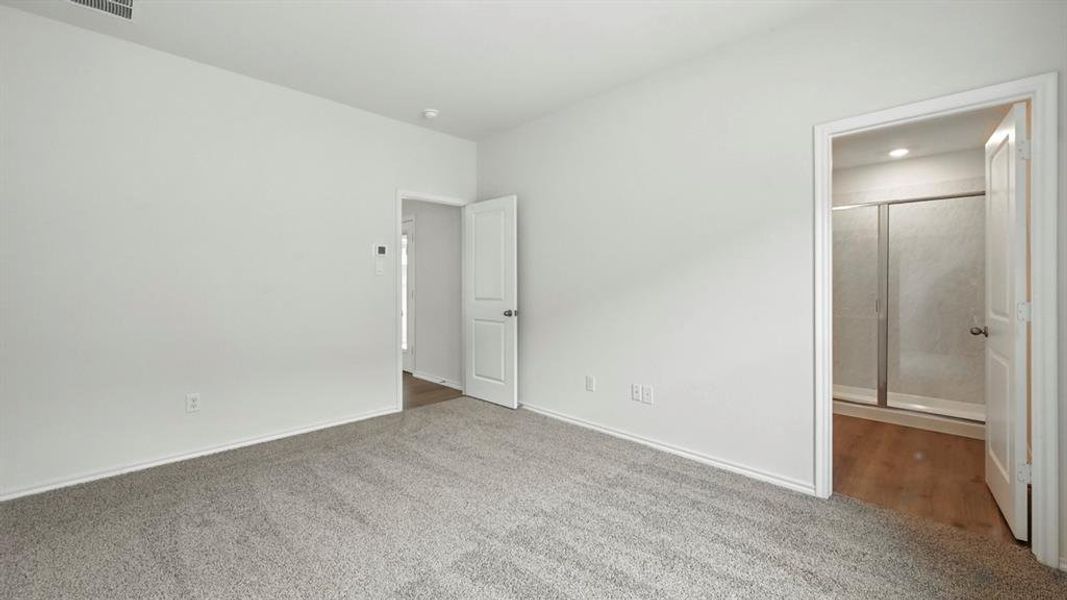 Carpeted room with a doorway leading to a bathroom featuring wood-finish flooring and a glass-enclosed shower Carpeted room with a doorway leading to a bathroom featuring wood-finish flooring and a glass-enclosed shower
