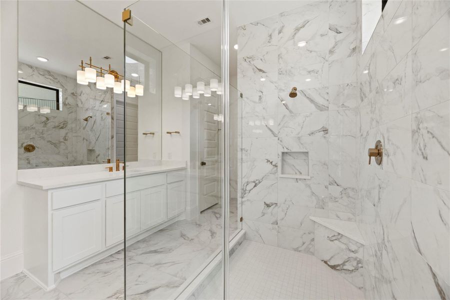 Expansive glass-enclosed shower wrapped in elegant floor-to-ceiling marble tile with a built-in seat and shower niche