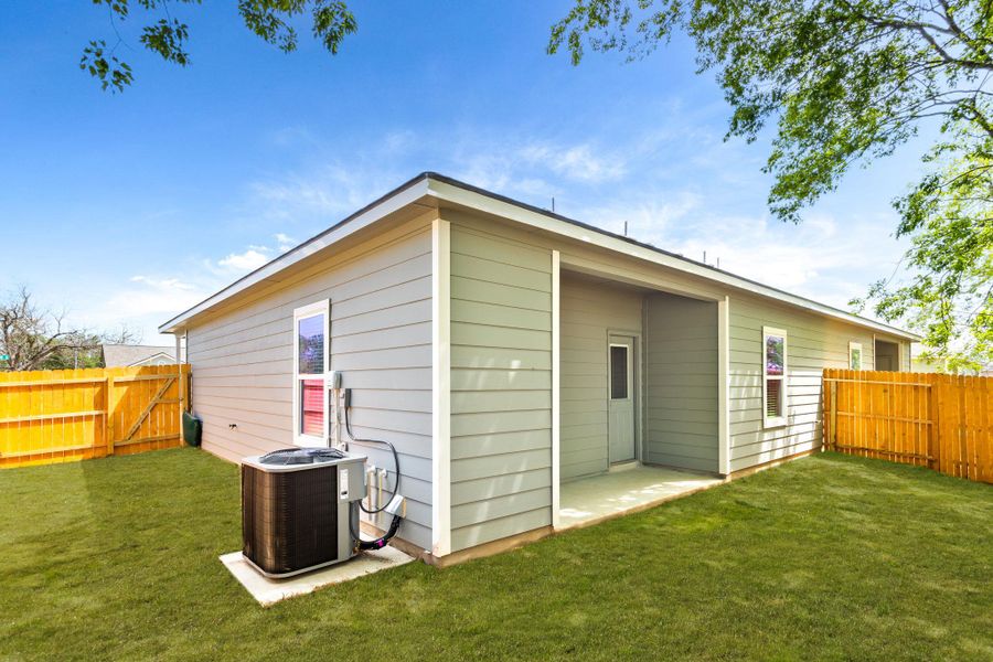 Rear exterior featuring light gray horizontal siding, a covered patio area with a white door, and a fenced yard