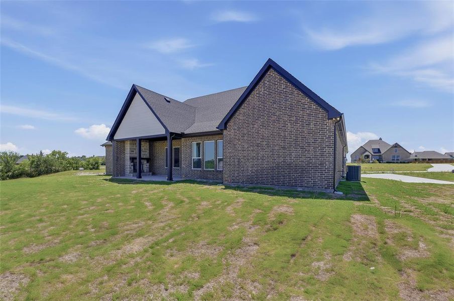 Rear exterior featuring a covered patio with a stone fireplace, dark brick facade, black trim, and multiple windows