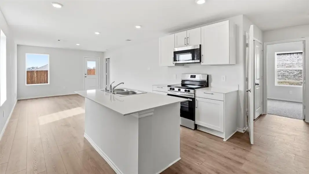 Kitchen featuring stainless steel appliances, white cabinets, a center island with sink, light wood-style flooring, and recessed lighting