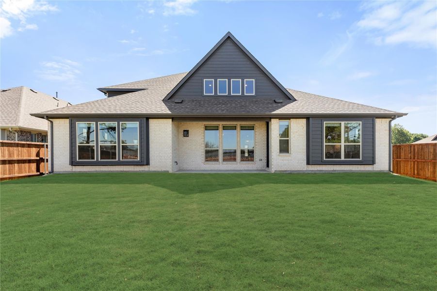 Rear exterior of home with white brick, dark gray siding, large windows, and fenced backyard with green lawn