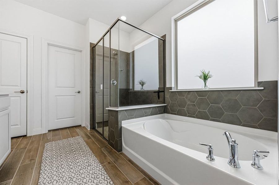 Primary Bathroom featuring a spacious soaking tub, a stand-up glass-enclosed shower, and a large window