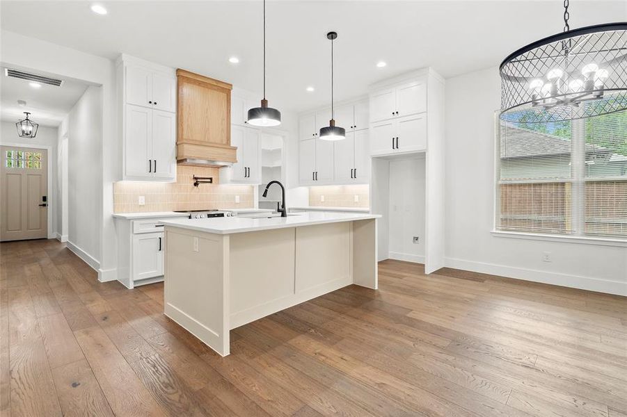 Open-concept kitchen and dining area featuring wide plank wood-finish flooring, white shaker cabinetry, a central island, and a decorative chandelier