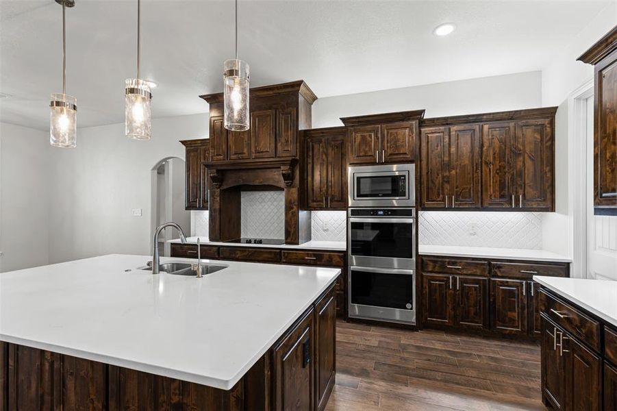 Kitchen with tasteful backsplash, dark brown cabinets, pendant lighting, arched walkways, and recessed lighting Kitchen with tasteful backsplash, dark brown cabinets, pendant lighting, arched walkways, and recessed lighting