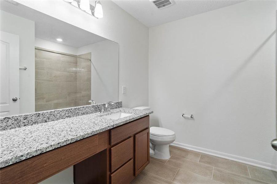 Secondary bath features tile flooring, bath/shower combo with tile surround, stained wood cabinets, beautiful light countertops, mirror, sleek fixtures and modern finishes.