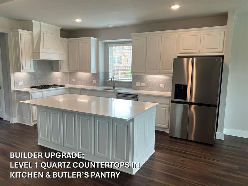 Gourmet kitchen featuring a large central island with quartz countertops, white shaker-style cabinetry, stainless steel appliances, a gas cooktop, and wood-finish flooring Gourmet kitchen featuring a large central island with quartz countertops, white shaker-style cabinetry, stainless steel appliances, a gas cooktop, and wood-finish flooring