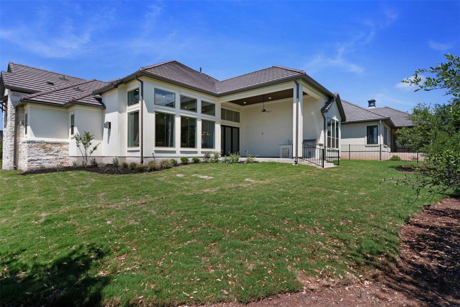 The property features an extensive lawn area, a covered patio with a ceiling fan, and large windows, providing ample natural light