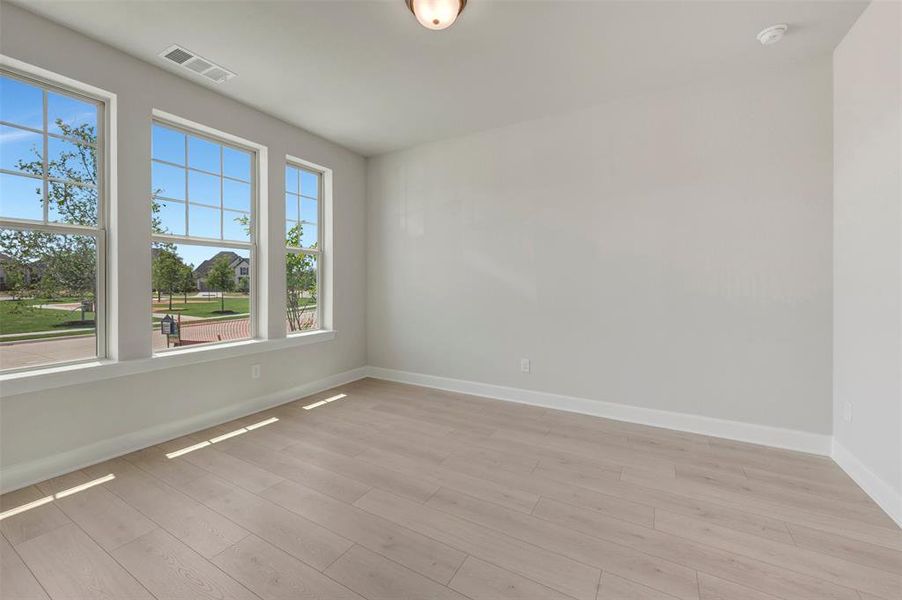Spacious room featuring three large windows, light wood-finish flooring, and light-toned wall paint