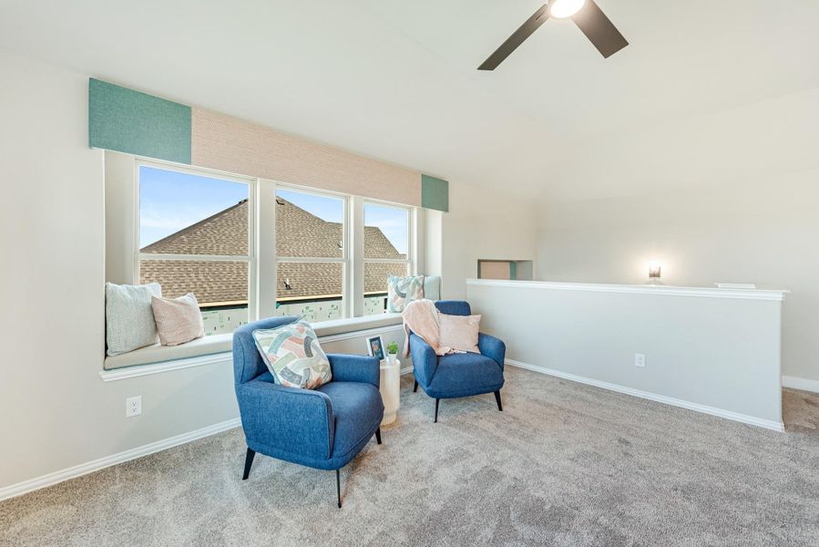 Sitting area with two blue chairs, window seat, vaulted ceiling, and ceiling fan on carpet flooring