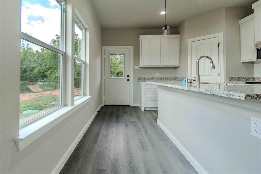 Kitchen featuring light stone counters, light hardwood / wood-style flooring, white cabinets, and decorative light fixtures