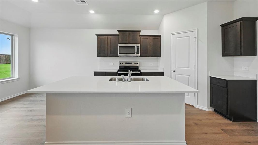 Kitchen featuring dark wood cabinetry, stainless steel appliances, a white tile backsplash, and light-colored countertops