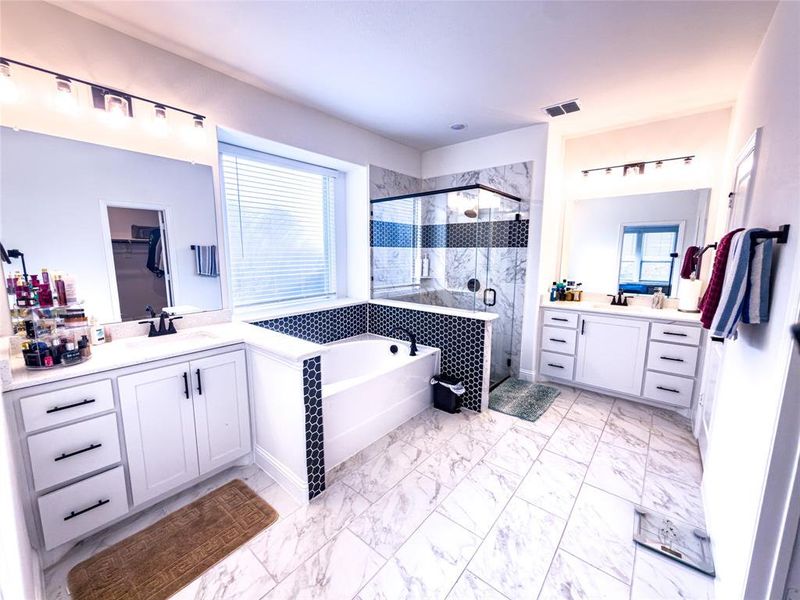 Bathroom featuring a shower stall, two vanities, a bath, light marble finish flooring, and healthy amount of natural light