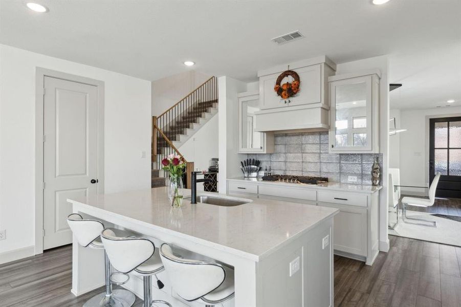 Kitchen with light stone countertops, a breakfast bar, dark wood finished floors, recessed lighting, and white cabinets Kitchen with light stone countertops, a breakfast bar, dark wood finished floors, recessed lighting, and white cabinets