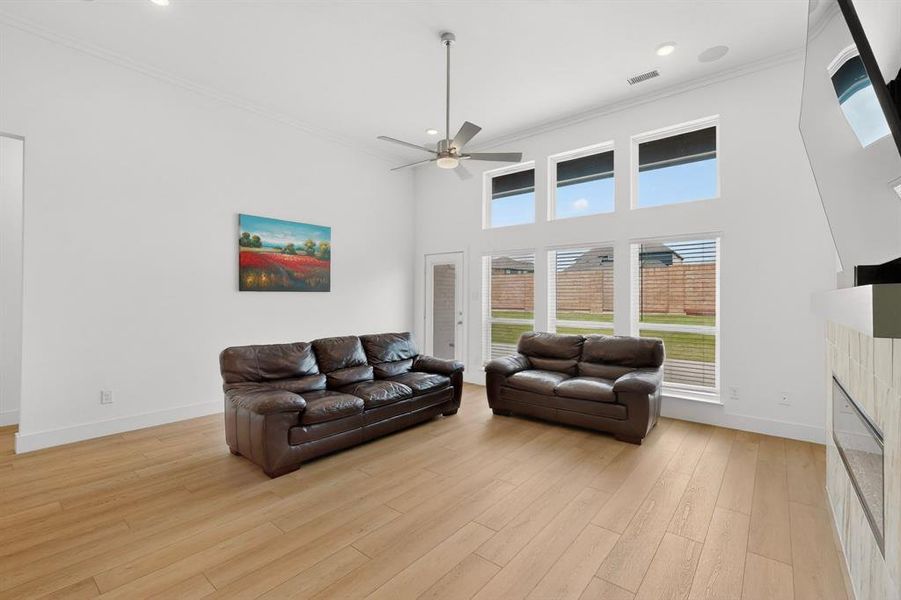 Living area featuring high ceilings, wood-finish flooring, a contemporary ceiling fan, and multiple large windows for abundant natural light Living area featuring high ceilings, wood-finish flooring, a contemporary ceiling fan, and multiple large windows for abundant natural light