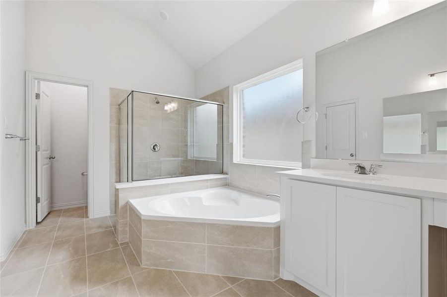 Spacious bathroom featuring a corner soaking tub, glass-enclosed shower, dual vanity with white cabinetry, large vanity mirror, and vaulted ceiling