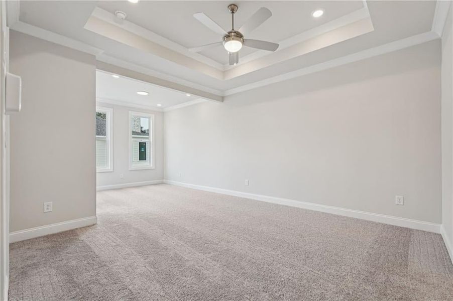 Spacious and open primary bedroom with sitting room, finished iwth crown molding, a ceiling fan, light colored carpet, and recessed lighting