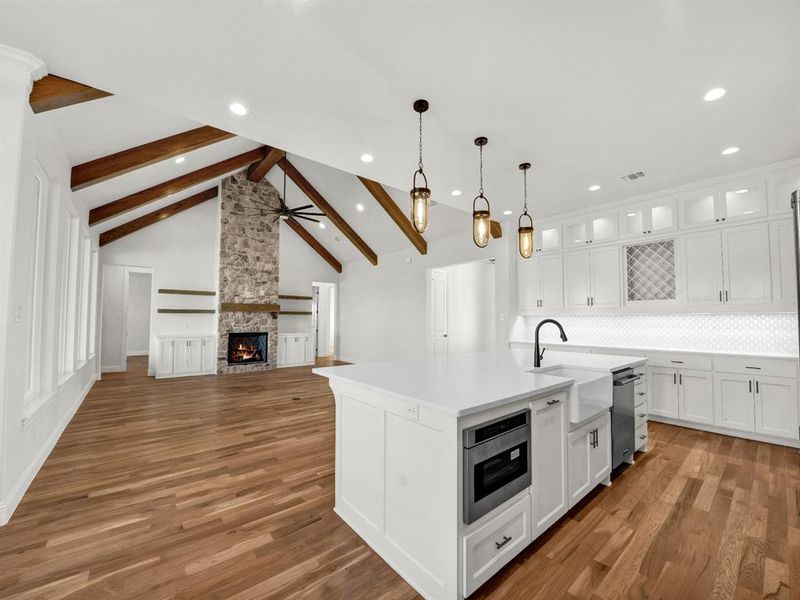 Kitchen featuring light wood-type flooring, a kitchen island with sink, sink, vaulted ceiling with beams, and white cabinetry