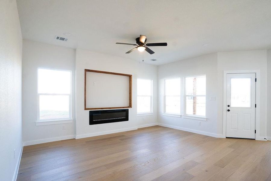 Unfurnished living room with a glass covered fireplace, ceiling fan, and light wood-style floors
