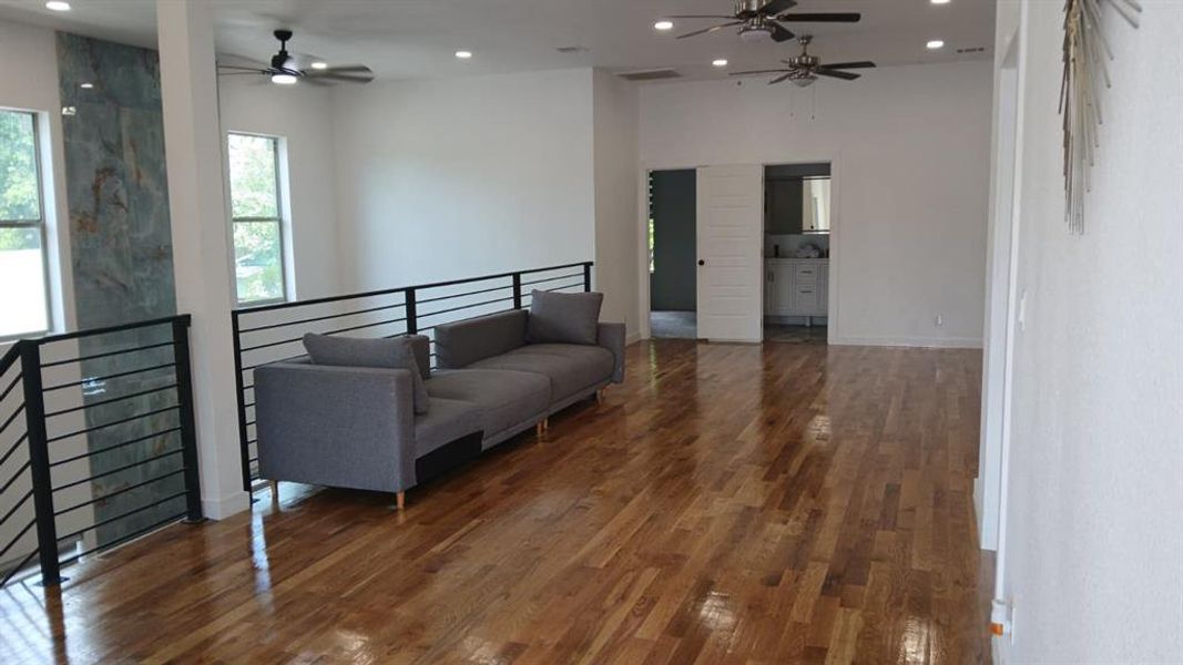 Spacious open-concept area featuring polished wood flooring, high ceilings with recessed lighting, and multiple ceiling fans