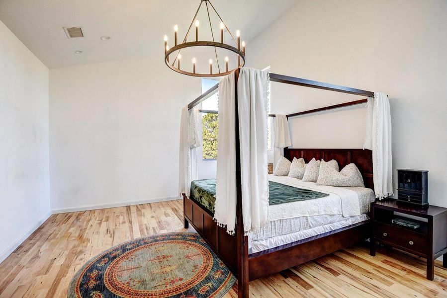 Bedroom with light wood-style flooring, a chandelier, and high vaulted ceiling Bedroom with light wood-style flooring, a chandelier, and high vaulted ceiling