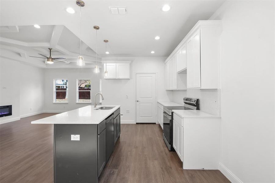 Kitchen with stainless steel appliances, sink, decorative light fixtures, a center island with sink, and white cabinets