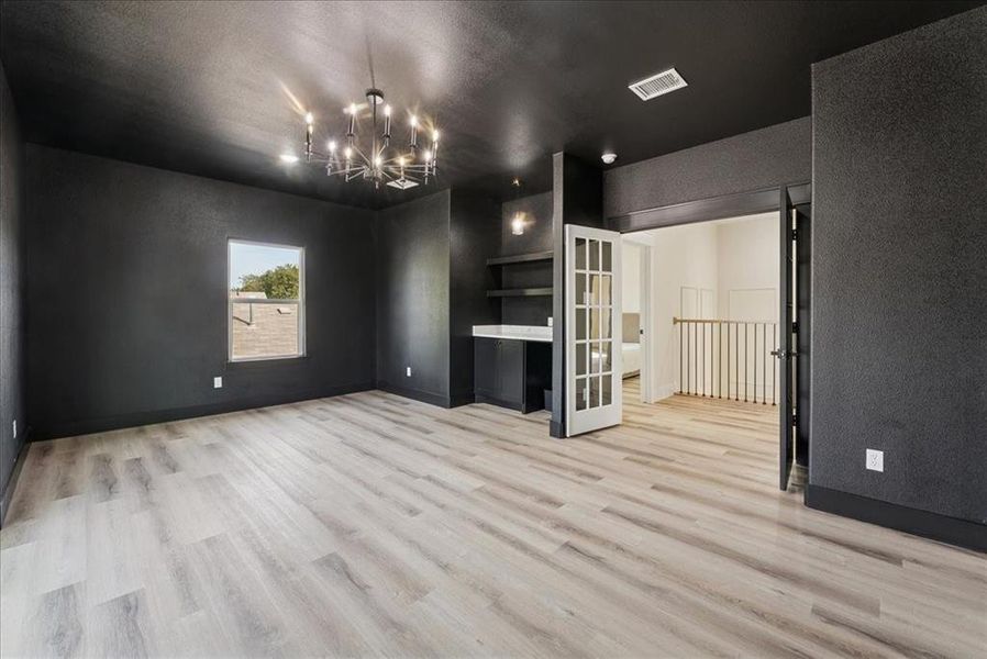 Unfurnished living room featuring light wood-style flooring, a chandelier, a textured ceiling, french doors, and a textured wall