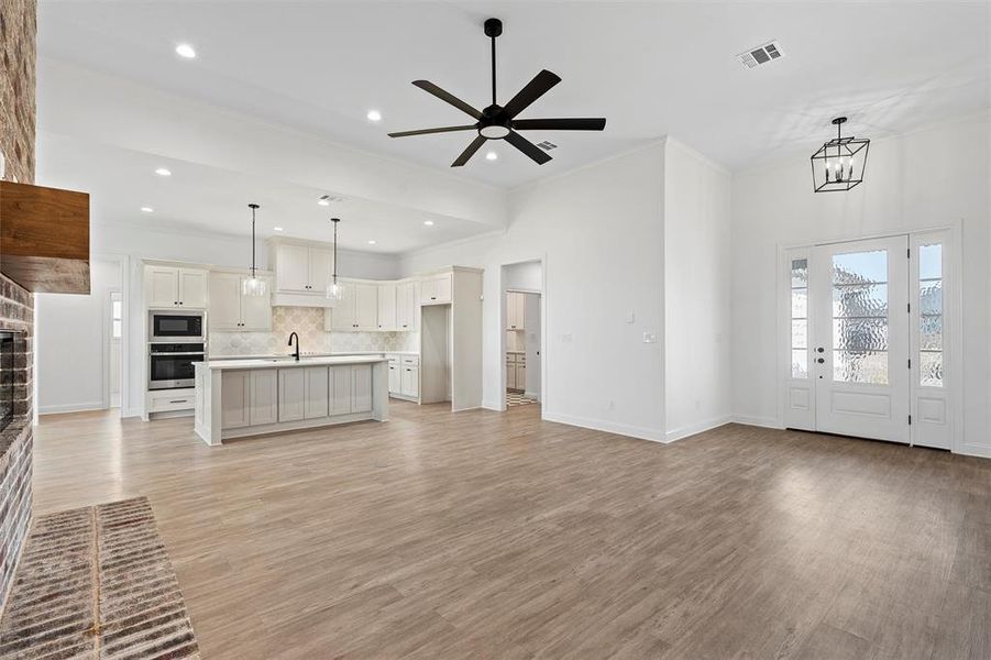 Unfurnished living room with crown molding, light wood finished floors, ceiling fan, recessed lighting, and a chandelier Unfurnished living room with crown molding, light wood finished floors, ceiling fan, recessed lighting, and a chandelier