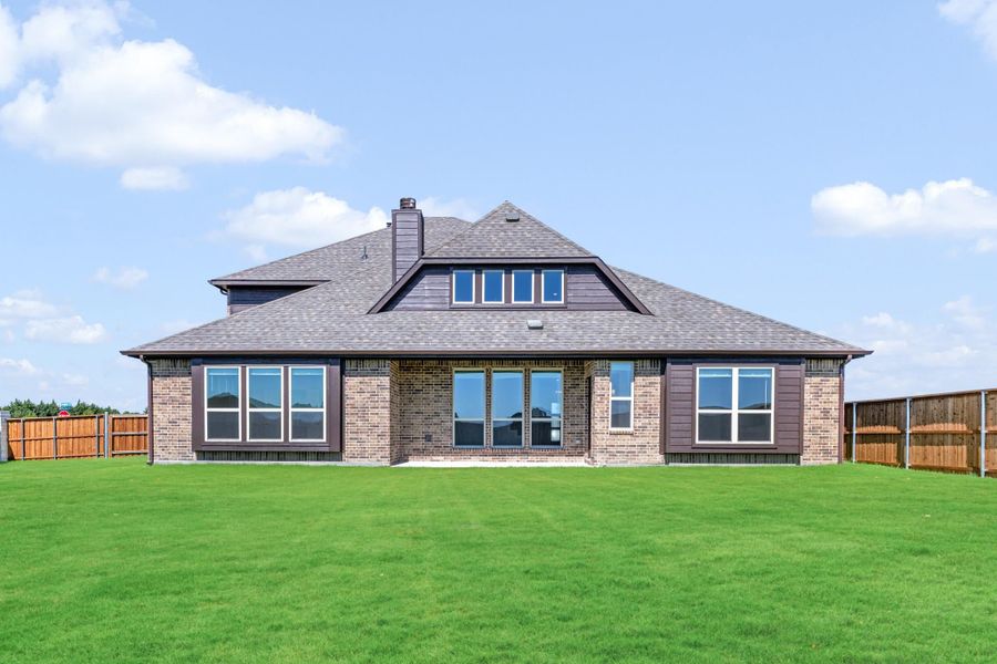 Rear view of brick home with large windows, hip roof, chimney, and fenced backyard with green lawn Rear view of brick home with large windows, hip roof, chimney, and fenced backyard with green lawn