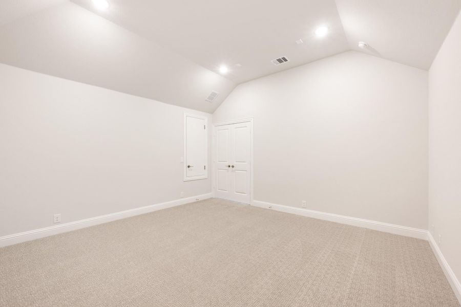 Empty bedroom with vaulted ceiling, recessed lighting, beige carpet, and two white doors