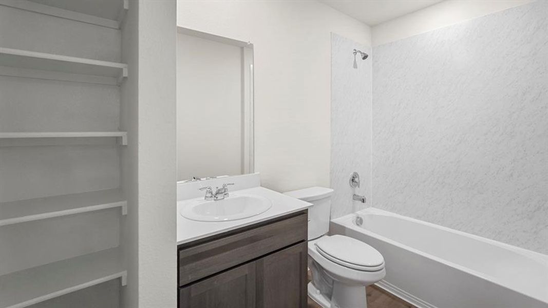 Bathroom featuring a single vanity with a white countertop and dark wood-finish cabinetry, a white bathtub with a shower, and integrated shelving