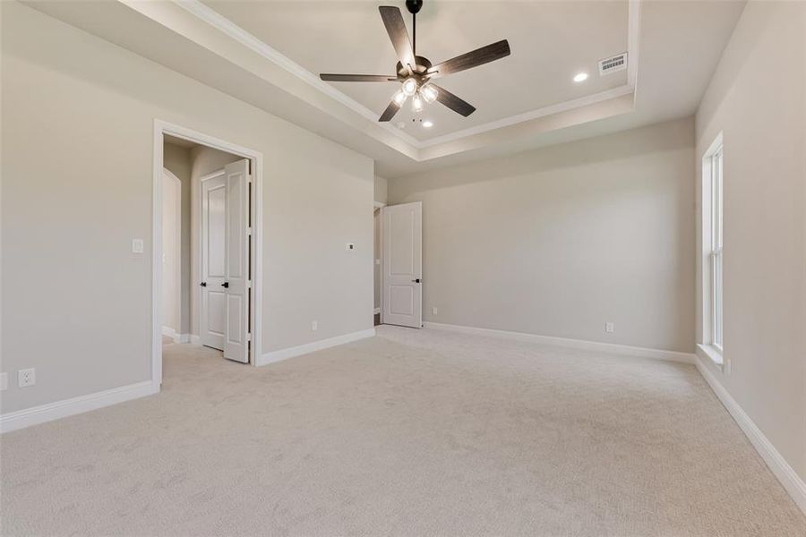 Empty room featuring a raised ceiling, recessed lighting, a ceiling fan, light carpet, and crown molding