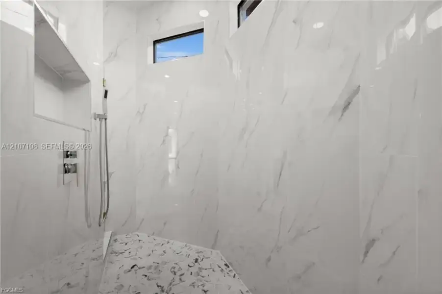 Walk-in shower featuring large-format stone-pattern wall tile, recessed built-in shelving, a handheld shower fixture, and clerestory windows