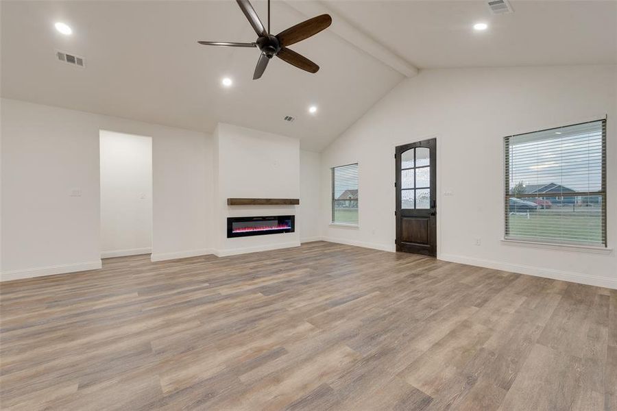 Unfurnished living room with beam ceiling, high vaulted ceiling, light wood-type flooring, and ceiling fan