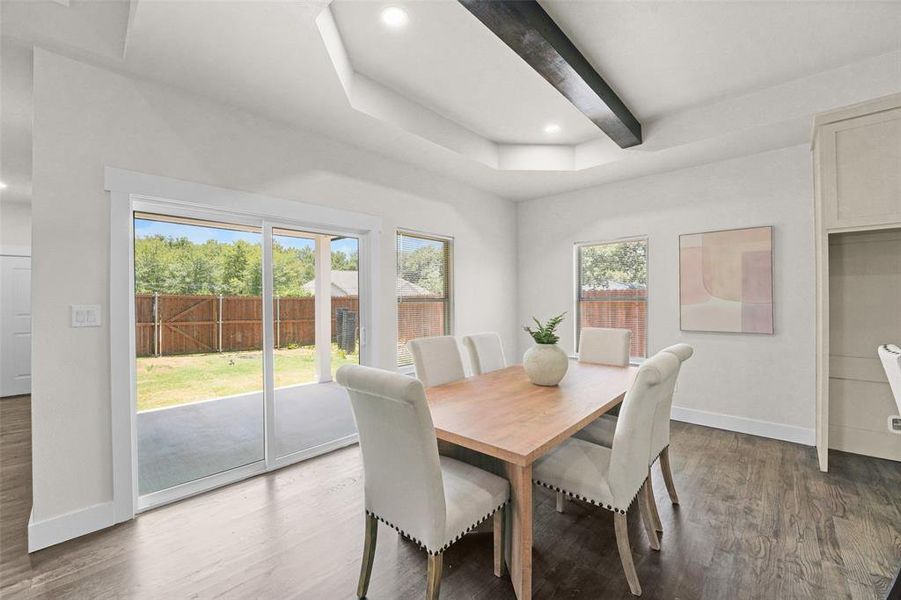 Dining area featuring wood-finish flooring, recessed lighting, and a tray ceiling with a dark wood beam accent Dining area featuring wood-finish flooring, recessed lighting, and a tray ceiling with a dark wood beam accent