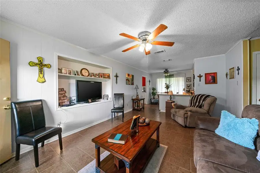 Living room with ceiling fan, ornamental molding, a textured ceiling, and tile patterned flooring