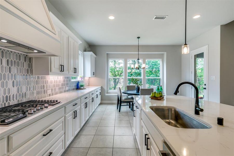 Kitchen featuring custom exhaust hood, stainless steel gas stovetop, pendant lighting, light tile floors, and sink