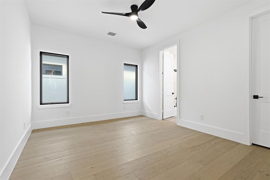 This bright bedroom showcases a minimalist design with crisp white walls and consistent wood-style flooring