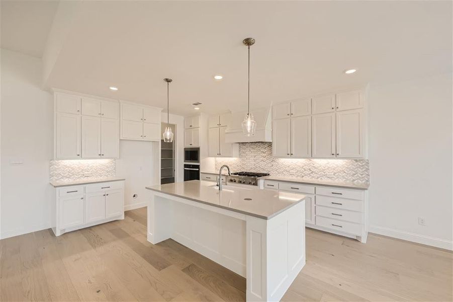 Kitchen with stainless steel appliances, light hardwood / wood-style flooring, white cabinets, a kitchen island with sink, and tasteful backsplash