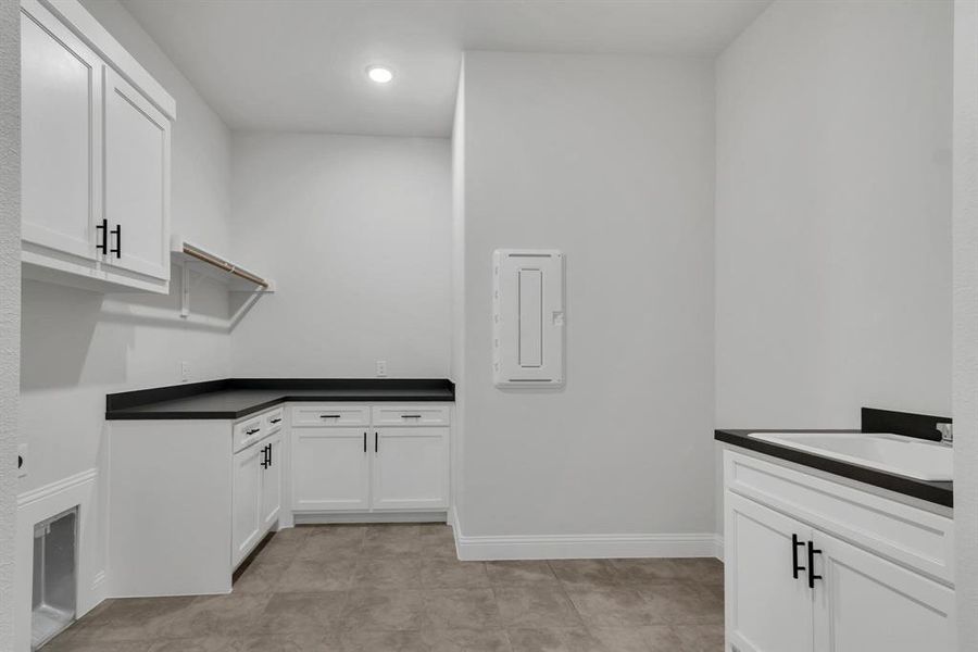 Laundry room featuring sink, light tile patterned flooring, and electric panel