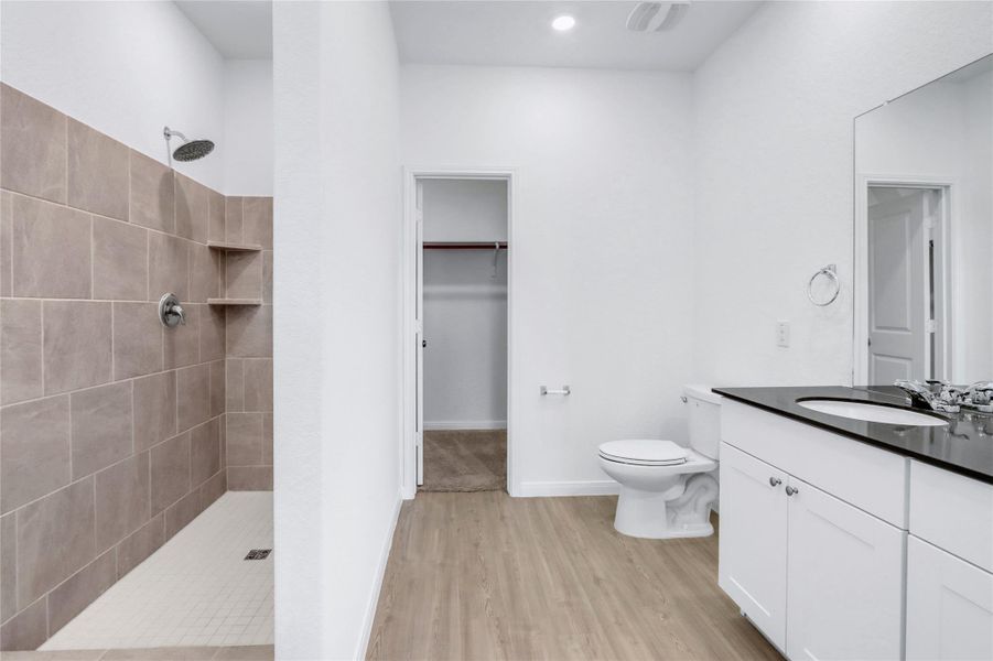 Bathroom featuring vanity, a walk in closet, tiled shower, and light wood-style floors